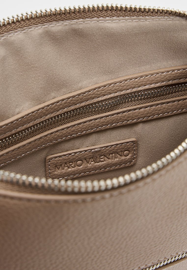 Intérieur d'un sac en cuir beige montrant un revêtement en tissu, une poche zippée et une étiquette cousue portant l'inscription "Mario Valentino" en relief.