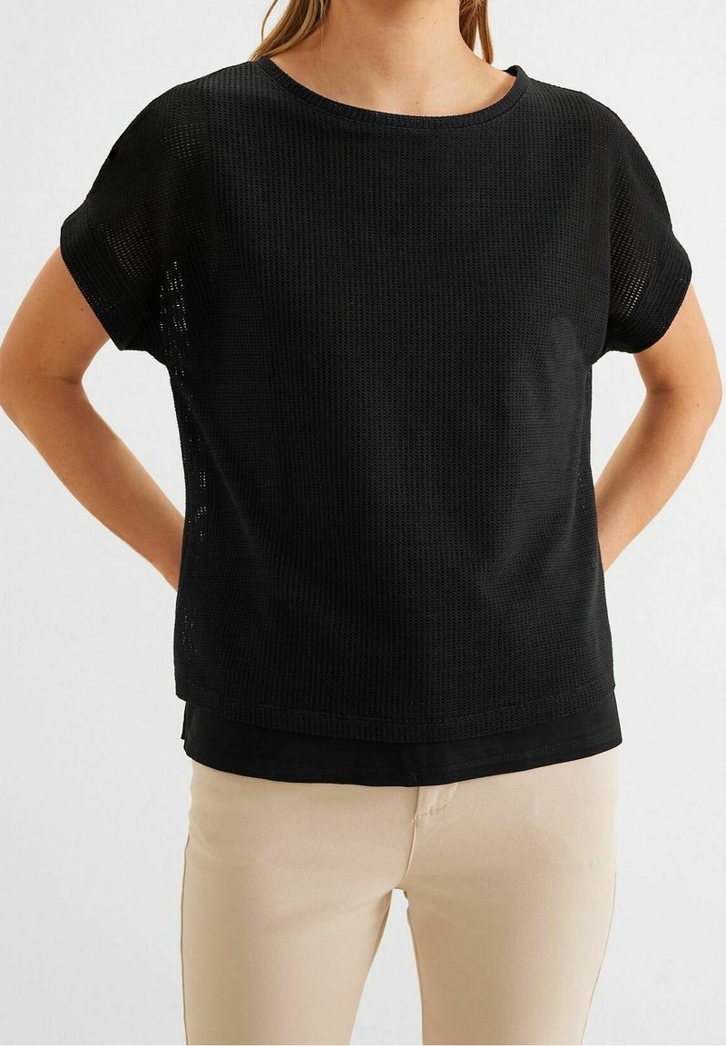 Svart kortärmad topp med en texturerad, ribbad design. Rund halsringning och lös passform, lager över en enfärgad svart nederkant.