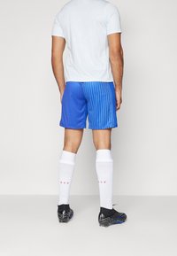 Blårandiga atletiska shorts med lös passform, tillsammans med vita knälånga strumpor med en rosa logotyp, och svarta fotbollsskor.