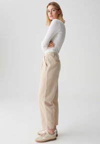 Beige Cordhosen mit lockerer Passform, ausgestattet mit seitlichen Taschen und einem Bund. Kombiniert mit hellen Sneakers mit strukturierten Akzenten.
