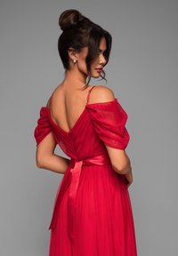 Robe rouge avec des manches bouffantes dénudées, texture plissée et un dos en V profond. Présente une ceinture en satin à la taille et une fermeture éclair.