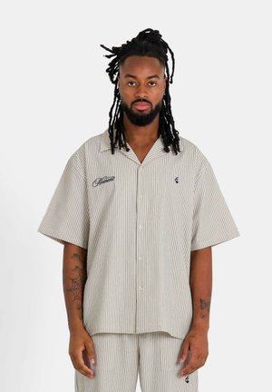 Camisa de manga corta a rayas en beige y blanco, con botones en la parte delantera y logotipos bordados en azul marino. Fabricada con tela ligera.