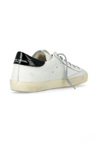 Baskets basses blanches avec languette de talon noire, lacets gris, semelle beige et texte "Philippe Model Paris" sur le talon, vues de côté arrière.