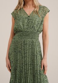 Abito verde con motivo, scollatura a V e maniche a cappuccio. Presenta una vita arricciata e una gonna plissettata, realizzato in tessuto leggero.