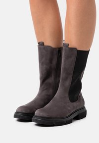 Stivali alla caviglia in suede grigio con una superficie liscia, dotati di pannelli laterali elasticizzati e chiusura con zip. La suola in gomma nera offre aderenza e durata.