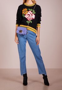 Suéter negro de punto con estampado floral, detalles en amarillo, jeans azul claro y botines negros con canalé en el tobillo. Bolso bandolera morado con cierre.
