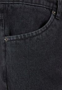 Černé džíny z denimu s klasickým designem, přední kapsou a kovovými detaily. Materiál je pevný a lehce drsný.