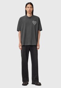 Camiseta de gran tamaño en gris oscuro con un gráfico de un corazón en gris más claro. Combinada con jeans negros holgados y calzado negro. Textura suave de algodón.