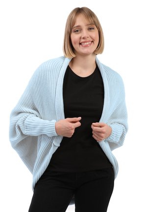 Jasnoniebieski, dzianinowy kardigan o szerokiej, luźnej sylwetce i prążkowanych mankietach. W zestawie z czarnym t-shirtem i czarnymi spodniami.