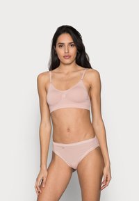 Bralette rosa claro com alças ajustáveis e um centro franzido. A lingerie correspondente apresenta um acabamento de renda e um pequeno detalhe de etiqueta.
