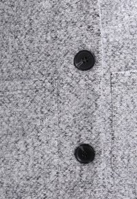 Šedá texturovaná tkanina s načechraným povrchem. Obsahuje černý knoflík a kapsu na náprsní straně. Jednoduchá barva bez vzorů.