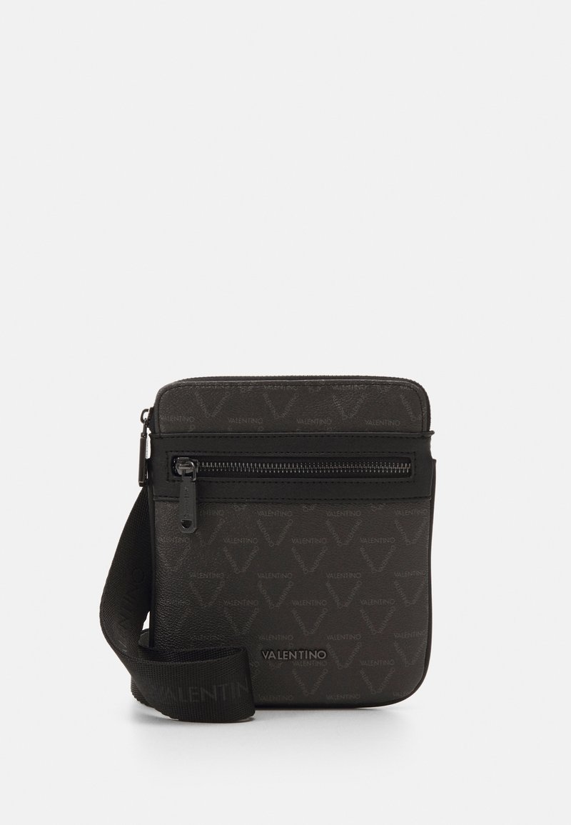 Sac bandoulière noir en matériau texturé avec un motif répétitif de logo, fermeture zippée et sangle en tissu ajustable.