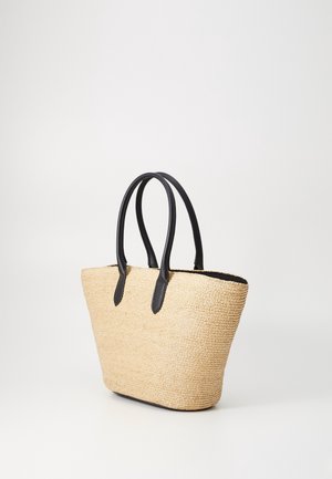 Borsa tote beige intrecciata con manici e rifiniture in pelle nera, in piedi su uno sfondo bianco semplice.