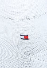 Chaussette de sport blanche avec un design texturé, comportant un petit logo brodé en rouge, blanc et bleu près de la cheville.