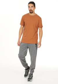 Brun bomullströja i kombination med grå sweatpants som har sidofickor, dragsko i midjan och elastiska mudd. Svarta och grå sneakers fulländar looken.