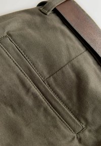 Roheline kangas sileda tekstuuriga, vertikaalse õmmeldud taskuga ja pruuni nahkrihmaga. Lihtne ja funktsionaalne disain.