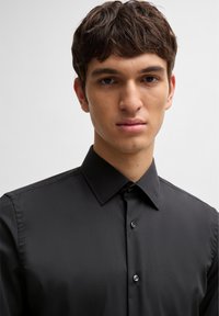 Black button-up shirt with a spread collar, smooth texture, and subtle sheen. Features buttons down the front and tailored fit.
