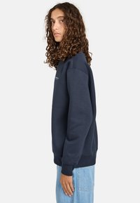 Felpa girocollo blu navy realizzata in tessuto morbido con polsini e orlo ribattuti. Presenta un piccolo logo sul petto e una vestibilità comoda.