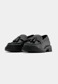 Black leather loafers with double tassel accents, rounded toe, low platform sole, and contrasting stitching details. Smooth texture throughout.