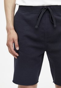 Pantaloni corti in felpa blu navy con vita elastica, chiusura con cordino, texture liscia e vestibilità comoda.