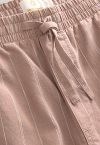 Lys lyserøde linnedshorts med hvide lodrette striber, udstyret med elastik i taljen og snøre. Blød tekstur, afslappet design.