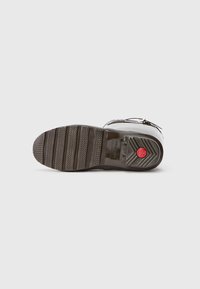 Suela de bota de goma negra con un patrón de tracción texturizado, que presenta un emblema rojo y un diseño de borde curvado para mejorar la adherencia.