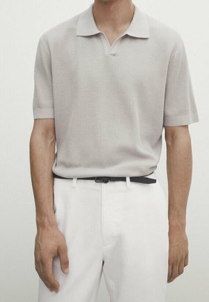 Polo shirt gris clair à manches courtes avec un motif en relief texturé et un col, associé à un pantalon blanc et une ceinture noire.