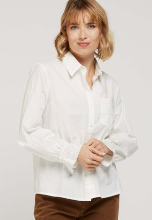 Chemise en coton blanc avec un devant à boutons, une petite poche poitrine et une bordure en œillets brodés aux poignets. Coupe décontractée, manches longues.
