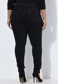 Černé skinny džíny s vysokým pasem, obsahující dvě zadní kapsy, akcenty zlaté barvy na knoflících a hladkou, elastickou tkaninu.