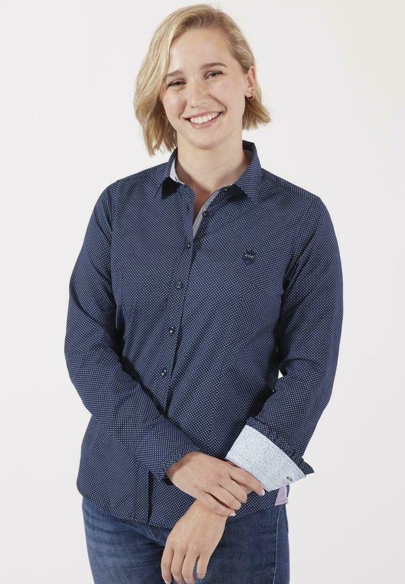Chemise boutonnée navy avec un petit motif de pois blancs, présentant des poignets bleu clair en contraste et un logo subtil sur la poitrine.
