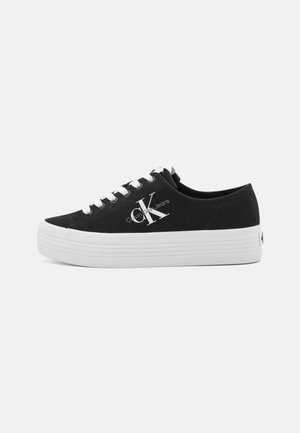 Black low-top sneaker with white thick platform sole, white laces, and large "CK Calvin Klein Jeans" logo on side.