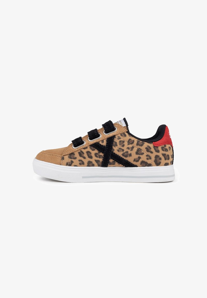 Zapatillas de estampado de leopardo con parte superior de ante color canela, correas de Velcro negras y una suela de goma blanca con un acento rojo en el talón.