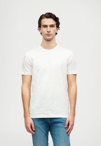 Tricou alb cu mânecă scurtă, cu un model floral texturat, guler rotund și țesătură moale, asortat cu blugi din denim albastru deschis.