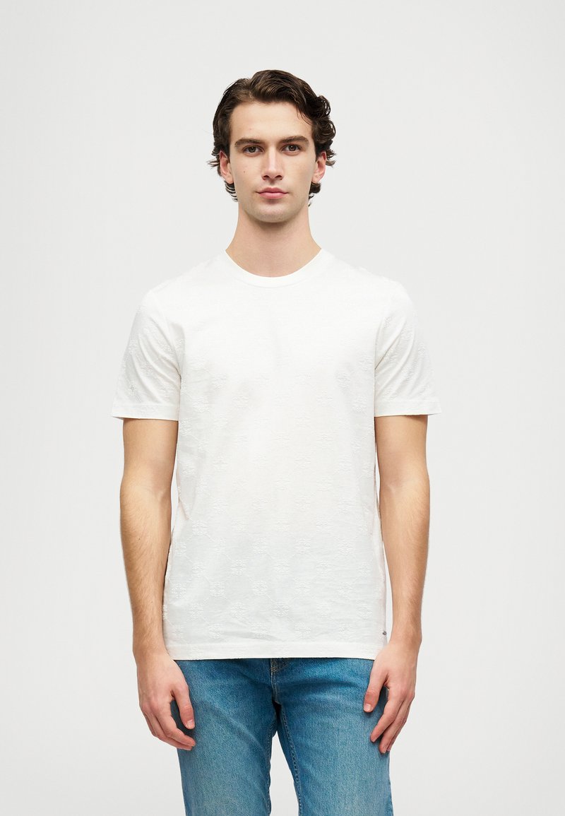 Tricou alb cu mânecă scurtă, cu un model floral texturat, guler rotund și țesătură moale, asortat cu blugi din denim albastru deschis.