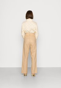 Blusa amarela estampada com um padrão redondo, calças beijas de cintura alta e sandálias de salto amarelas, vistas por trás contra um fundo branco.