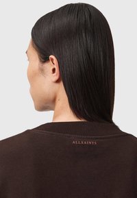 Ruskea huppari, jossa on ribattu kaulus ja hihansuut. Takana kaulassa näkyy erivärinen "ALLSAINTS"-logo. Silkkinen pinta.