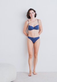 Soutien-gorge en dentelle bleue et culotte assortie avec un bord festonné et des détails délicats. Le tissu semble doux avec une texture lisse.