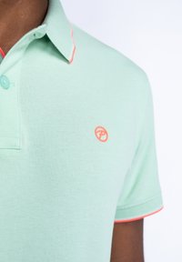 Miętowa koszulka polo z teksturowanej tkaniny, z kołnierzykiem na dwa guziki oraz kontrastowym koralowym wykończeniem na kołnierzyku i rękawach, logo na piersi.