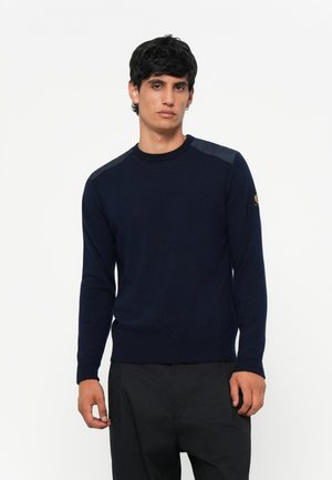 Navy blue knitted sweater with long sleeves, round neckline, and contrasting textured shoulder accents. Fitted at the waist and cuffs.
