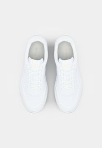 White leather sneakers with rounded toe, laces, and subtle Lacoste branding on the tongue and side. Smooth texture and minimalist design.
