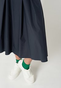 Falda de tela de marina con pliegues, combinada con zapatillas blancas y calcetines verdes. La falda presenta un diseño fluido con una textura suave y un drapeado suave.