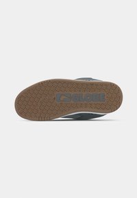 Grijze sneaker met een gelamineerde rubberen zool, uitgerust met een logo en een patroon van kleine vierkantjes. Geaccentueerd met een witte streep aan de zijkant.