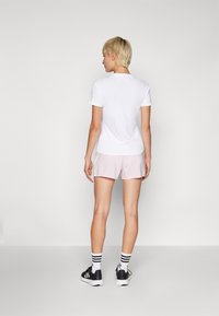 Hvit tettsittende t-skjorte og lyserosa shorts, med svarte joggesko. Funksjoner inkluderer korte ermer og stripete hvite og svarte sokker.