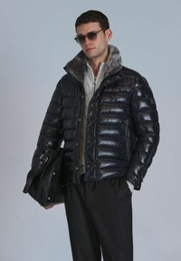 Glänzende dunkelblaue Daunenjacke mit einem Kunstfellkragen, Frontknöpfen und seitlichen Taschen. Gestylt mit einem grauen Pullover und einer schwarzen Ledertasche.