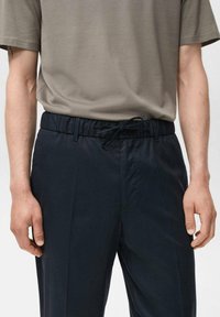Marineblauwe broek met elastische tailleband en trekkoord. Gedragen met een lichtgrijs overhemd met korte mouwen. Het materiaal lijkt glad en lichtgewicht.