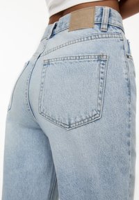 Vaqueros de mezclilla azul claro con una cintura alta, que presentan una tela texturizada, dos bolsillos traseros y una etiqueta de cuero marrón con la marca en la cinturilla.