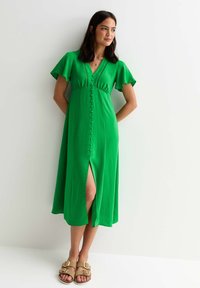 Vestido midi verde con mangas acampanadas, escote en V, detalles de botones en la parte delantera y una abertura lateral, confeccionado en una tela ligera. Corte casual.
