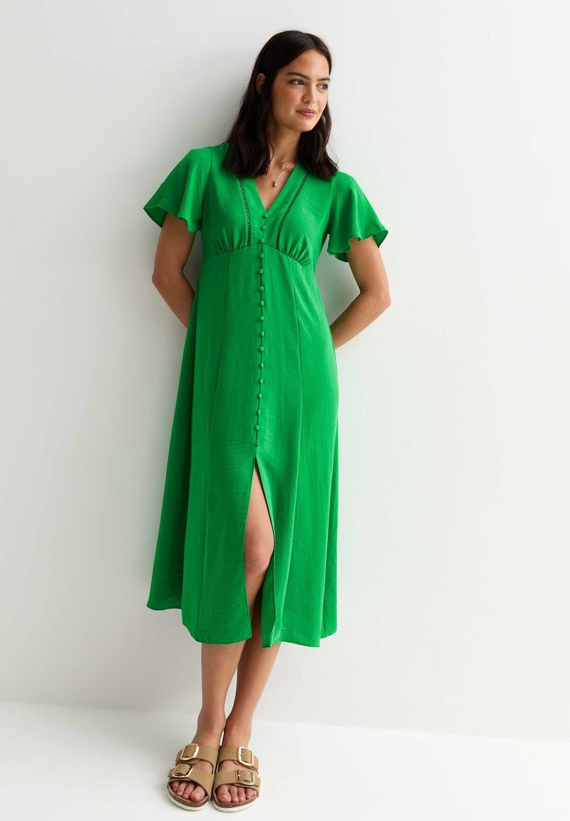 Vestido midi verde con mangas acampanadas, escote en V, detalles de botones en la parte delantera y una abertura lateral, confeccionado en una tela ligera. Corte casual.