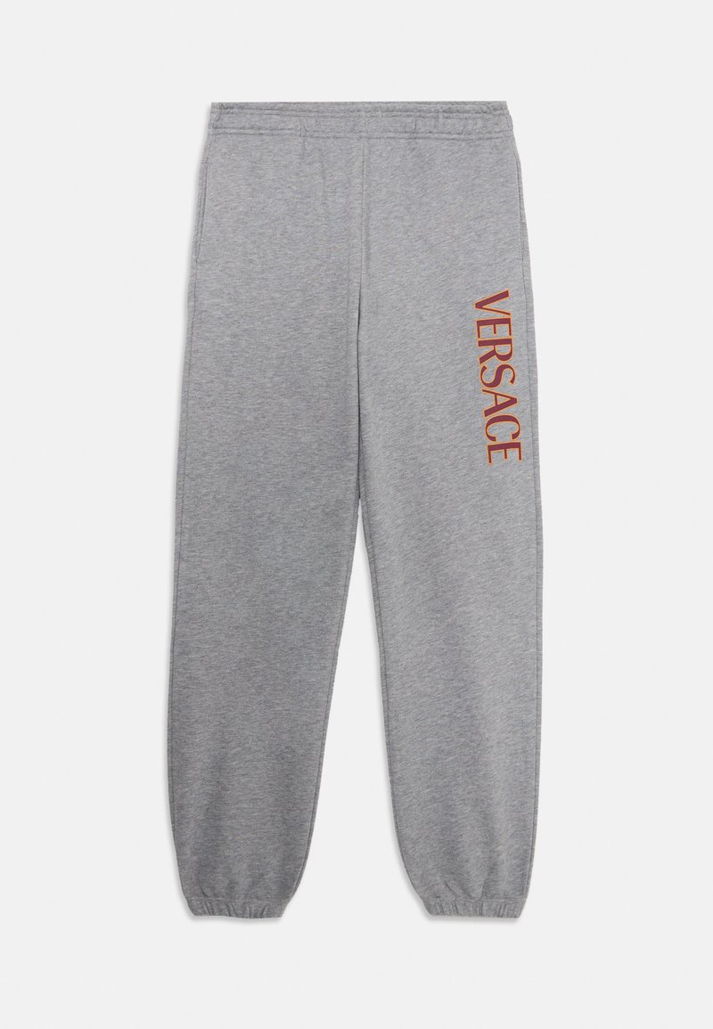 šedé tepláky vyrobené z mäkkej tkaniny, s elastickým pásom a manžetami na členkoch, s potlačou "VERSACE" v oranžovej farbe na ľavej nohe.