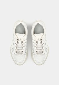 Valged spordijalatsid tekstuurse pealmise osa, võrgust paneelide ja helkivate detailidega. Omavad paeltega kinnitamist ja polsterdatud tallaga.